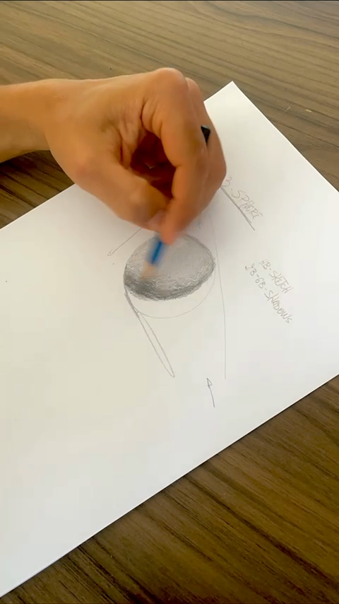 A hand builds a shaded sphere drawing on paper